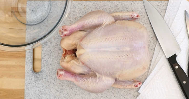 Using kitchen knife to cut raw chicken leg away from flesh