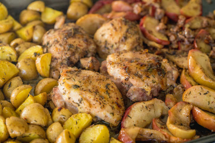 Close up of seasoned chicken thighs, potatoes, and apple slices