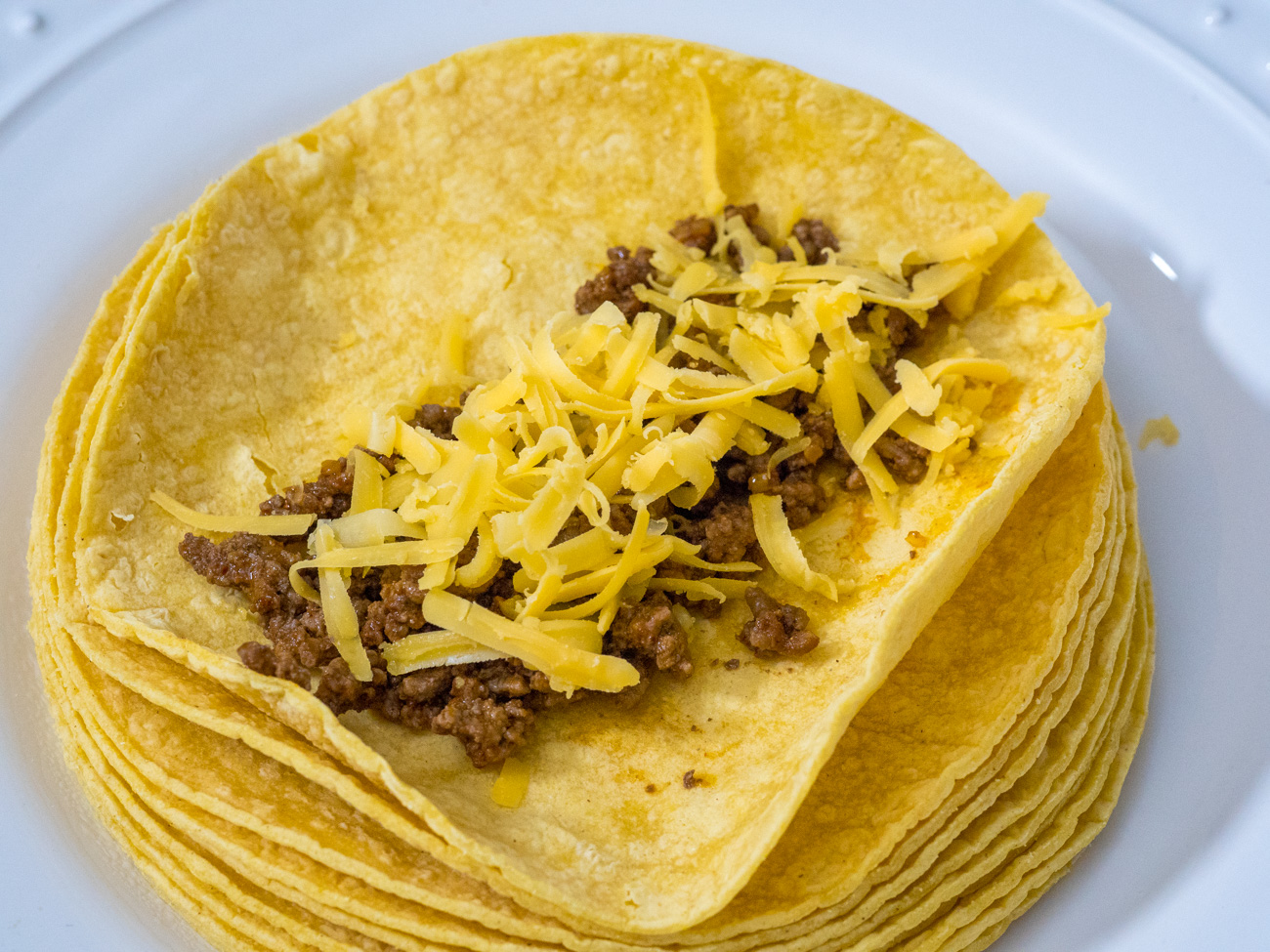 Place some of the ground beef and some of the cheddar in a straight line in the center of each tortilla and roll tightly.