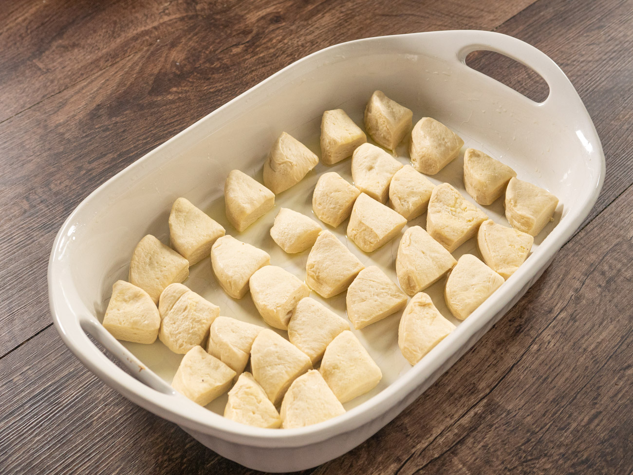 Cut biscuits into quarters and arrange evenly in the baking dish. Layer frozen vegetables and shredded cheeses on top of the biscuits and set aside.