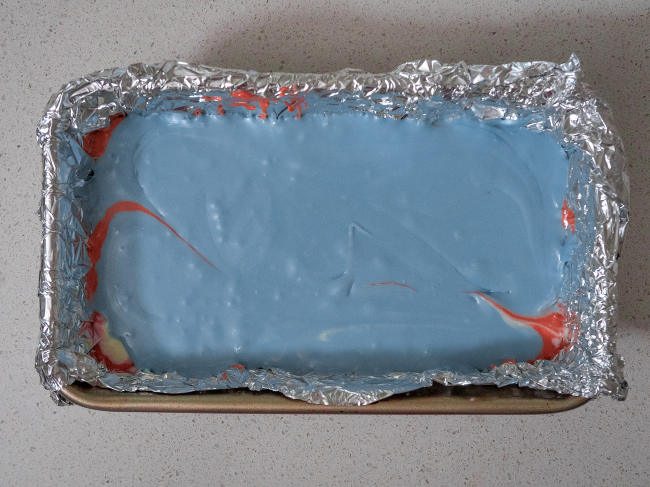 Pour the fudge into the loaf pan in layers in the order of red, white, and finally blue. Smooth each layer with the back of a clean spoon.