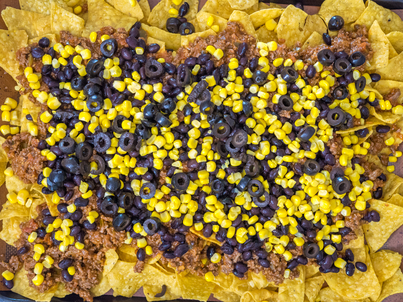Top with ground beef mixture, black beans, corn, olives, and cheese.