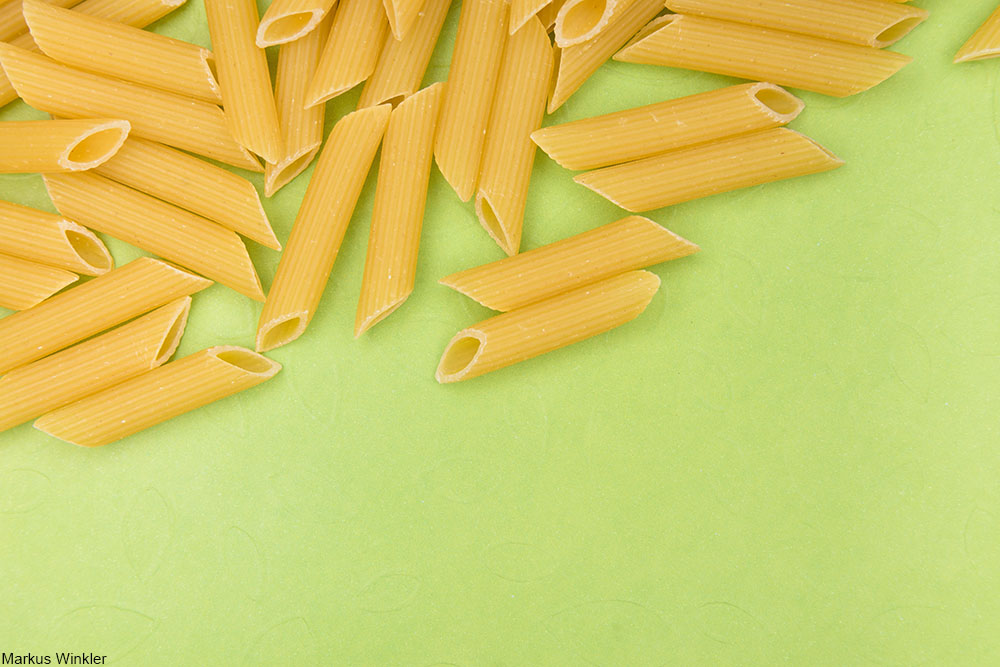 dried penne pasta on green background