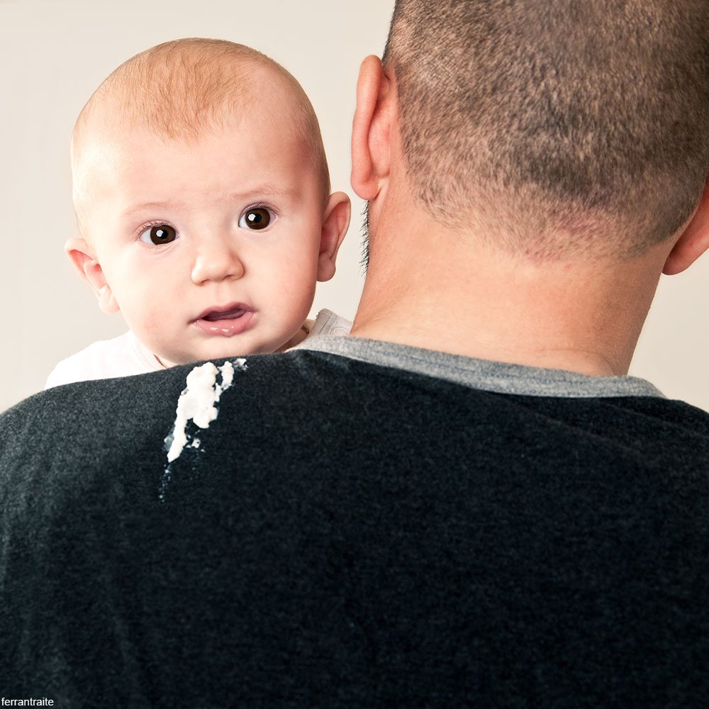 baby throwing up on man's shoulder