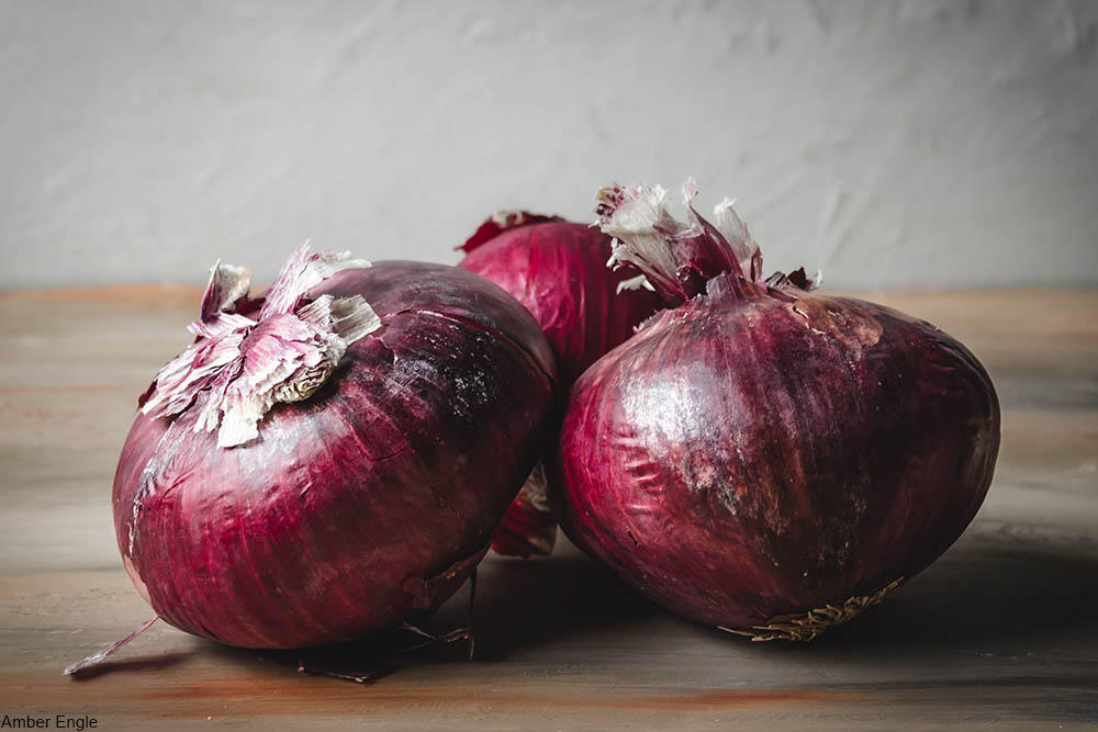 three red onions on a cutting board