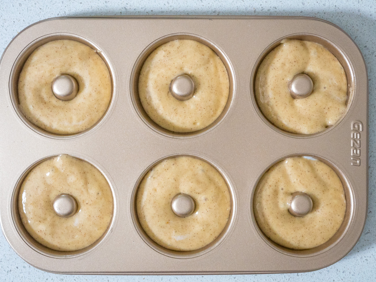 Lepelbeslag in een zak met glaspijp of een plastic zak met ritssluiting waarvan het uiteinde is afgesneden voor het gemakkelijk vullen van donutvormpan. Vul elk deel van de donutpan ongeveer 75% vol met beslag.