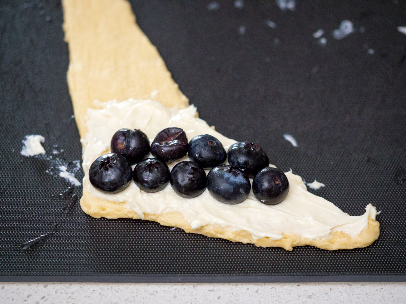 Separate canned crescent rolls into 8 triangles along the perforated seams. Place a triangle of dough on a clean, flat surface, with the short, wide end facing you and the long triangle pointing away. Spread a tablespoon of cream cheese mixture across the bottom third of the dough triangle. Top the cream cheese with two rows of blueberries.