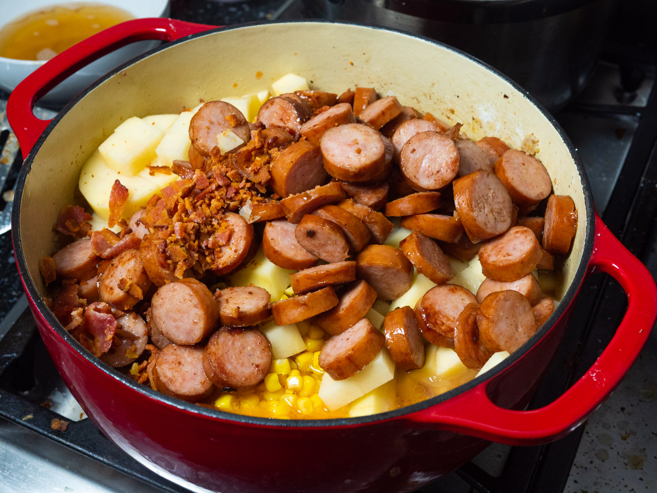 Add tomatoes, baked beans, green chiles, corn, potatoes, bacon, sausage, and water. Bring to a boil, then reduce heat and simmer, covered for about an hour, stirring occasionally.