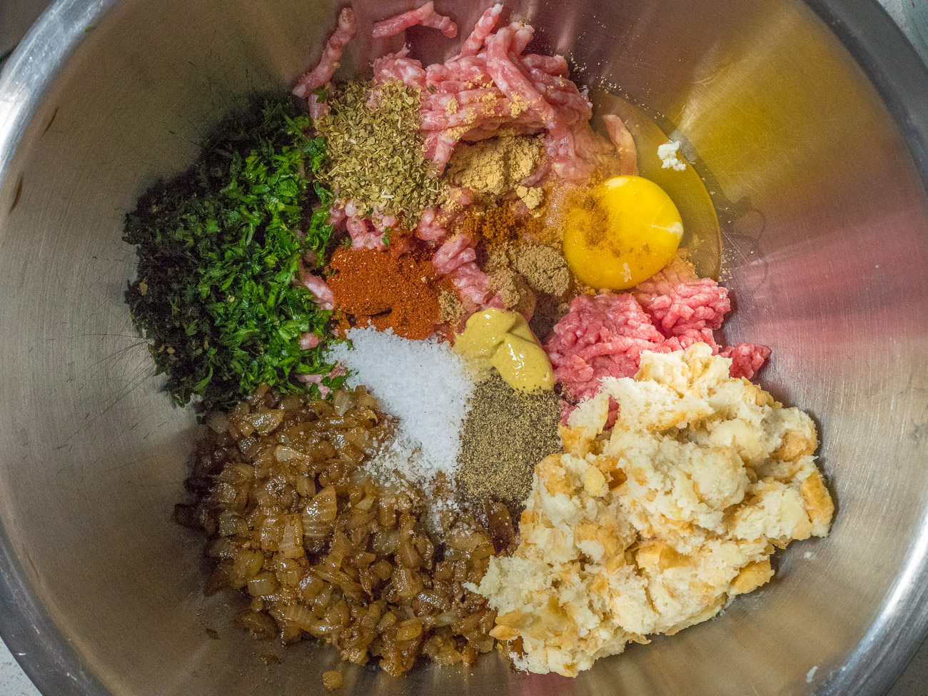 Place onions and garlic in a bowl along with bread, beef, pork, egg, parsley, salt, pepper, yellow mustard, oregano, paprika, ginger, mace, and coriander and stir.