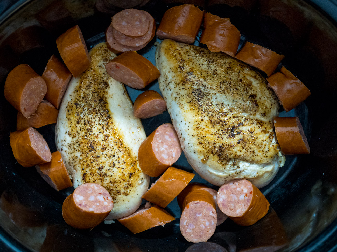 Place chicken breasts in the slow cooker, along with sausage, heavy cream, chicken broth, butter, garlic cloves, cajun seasoning, and a sprinkle of salt & pepper.