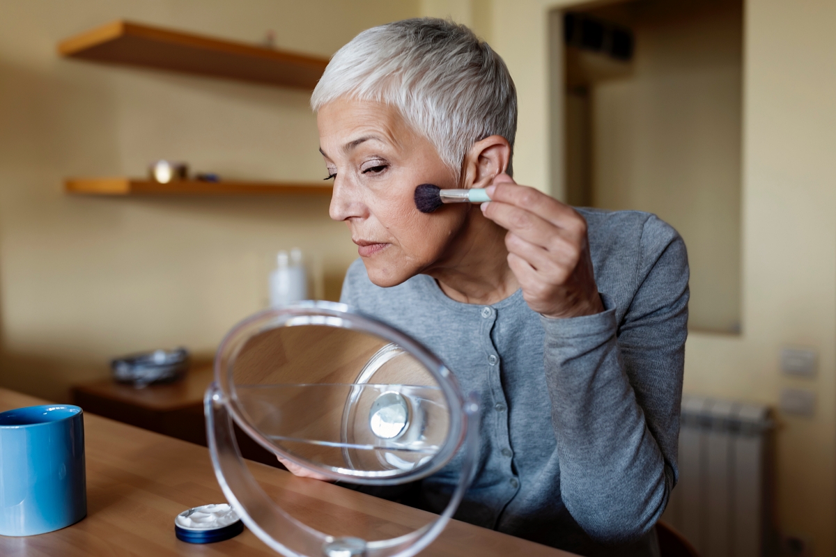 woman with grey hair applying blush to her cheeks