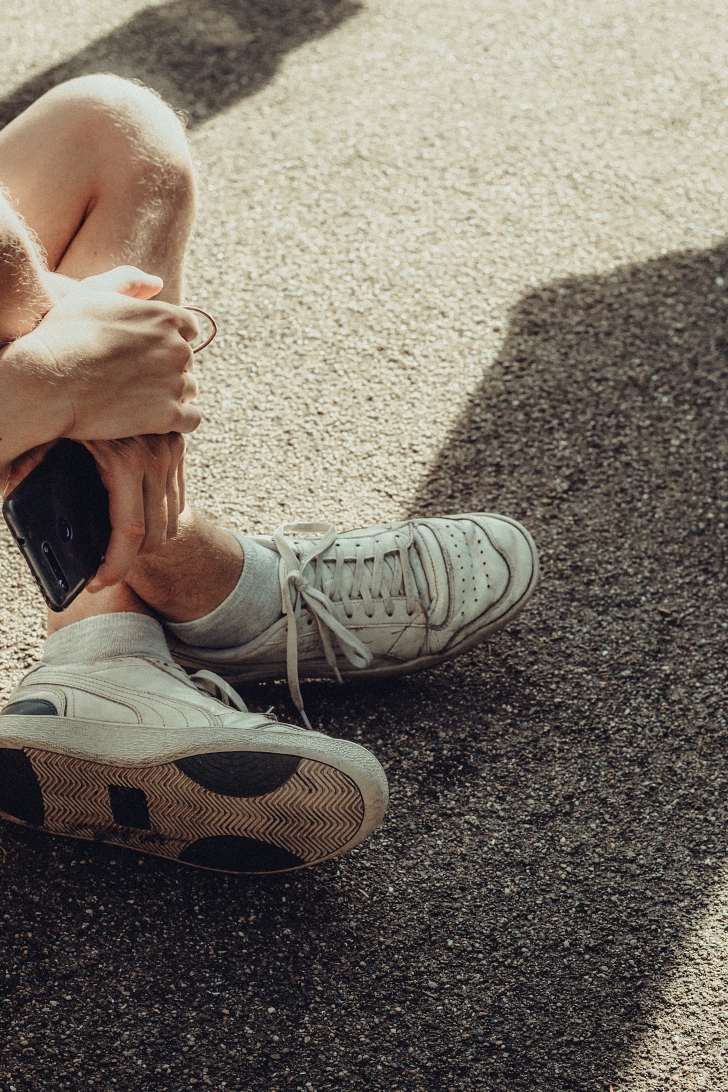 person with worn sneakers sitting on ground