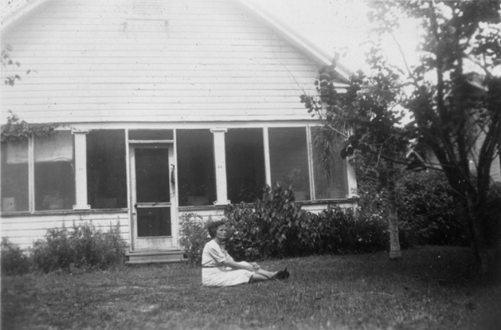 woman sitting on the ground in front of a house, 1940s
