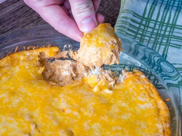 Close up of dish with baked cheese on top, dipping a chip into the sauce