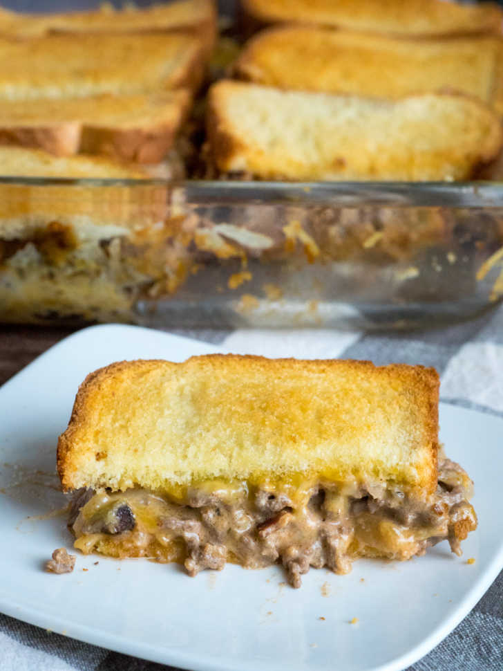 Photo of grilled cheese sandwich cut in half with meat sauce in the middle. Casserole dish in the background.