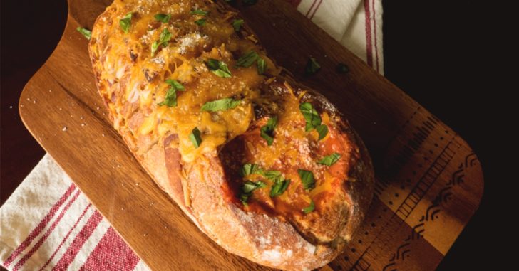 A loaf of bread with a hole cut out on one end like a bowl, holding tomato soup.