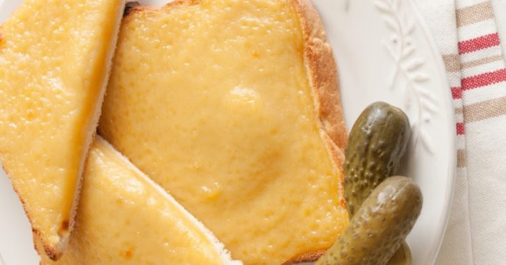 Two triangles of bread with cheese sauce and pickles on the side.