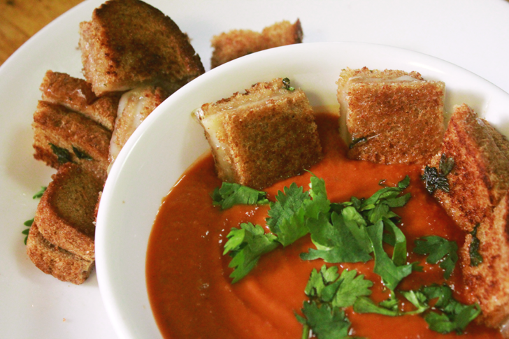 Top down image of a bowl of tomato soup with little square grilled cheese sandwiches as croutons.