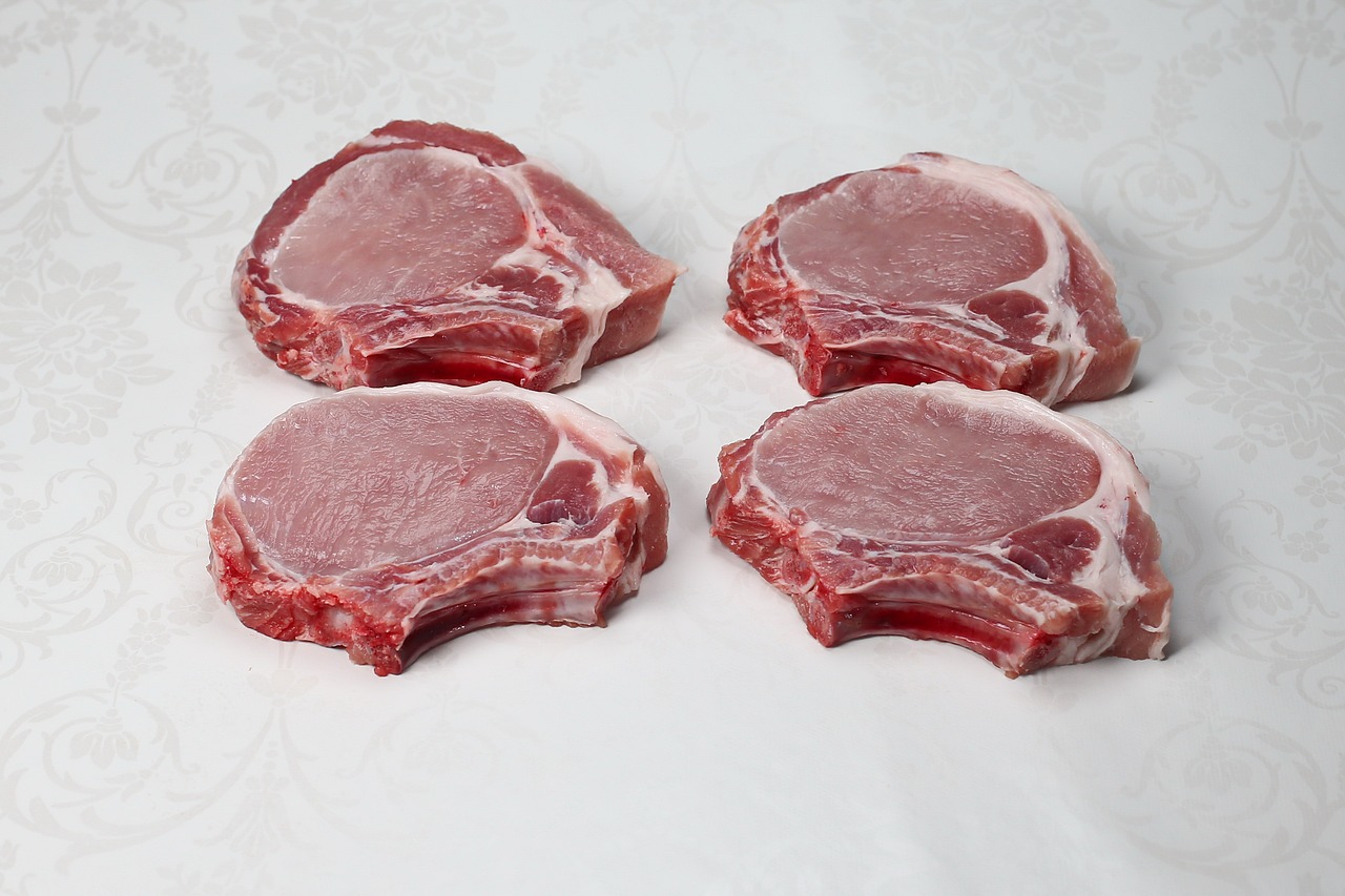 Four raw pork chops on a white background.