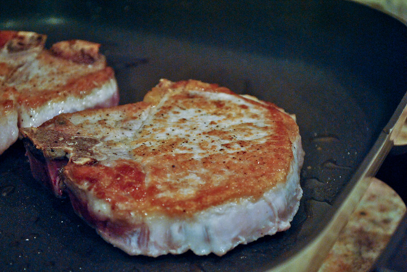 Close up of pork chop in a skillet, slightly browned on top.