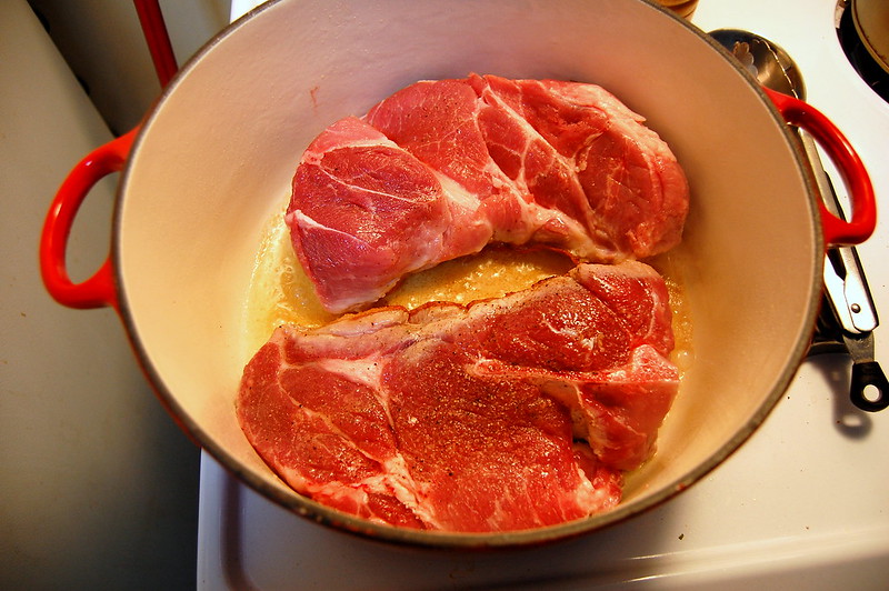 Two raw pork shoulders in a dutch oven.