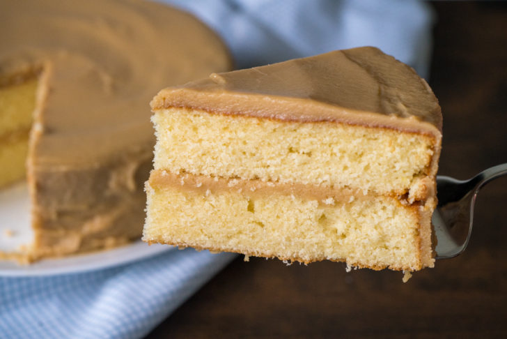 Slice of caramel cake being taken out of the whole cake.