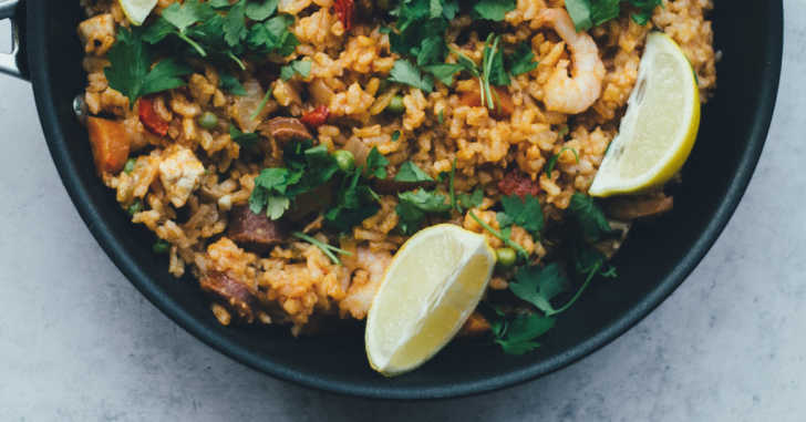 Top down of rice and kale in a skillet with lemon wedges