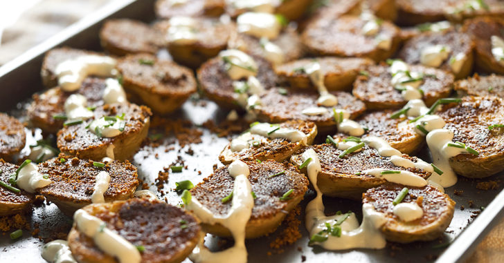 Potato slices on a sheet pan with creamy sauce drizzled on top