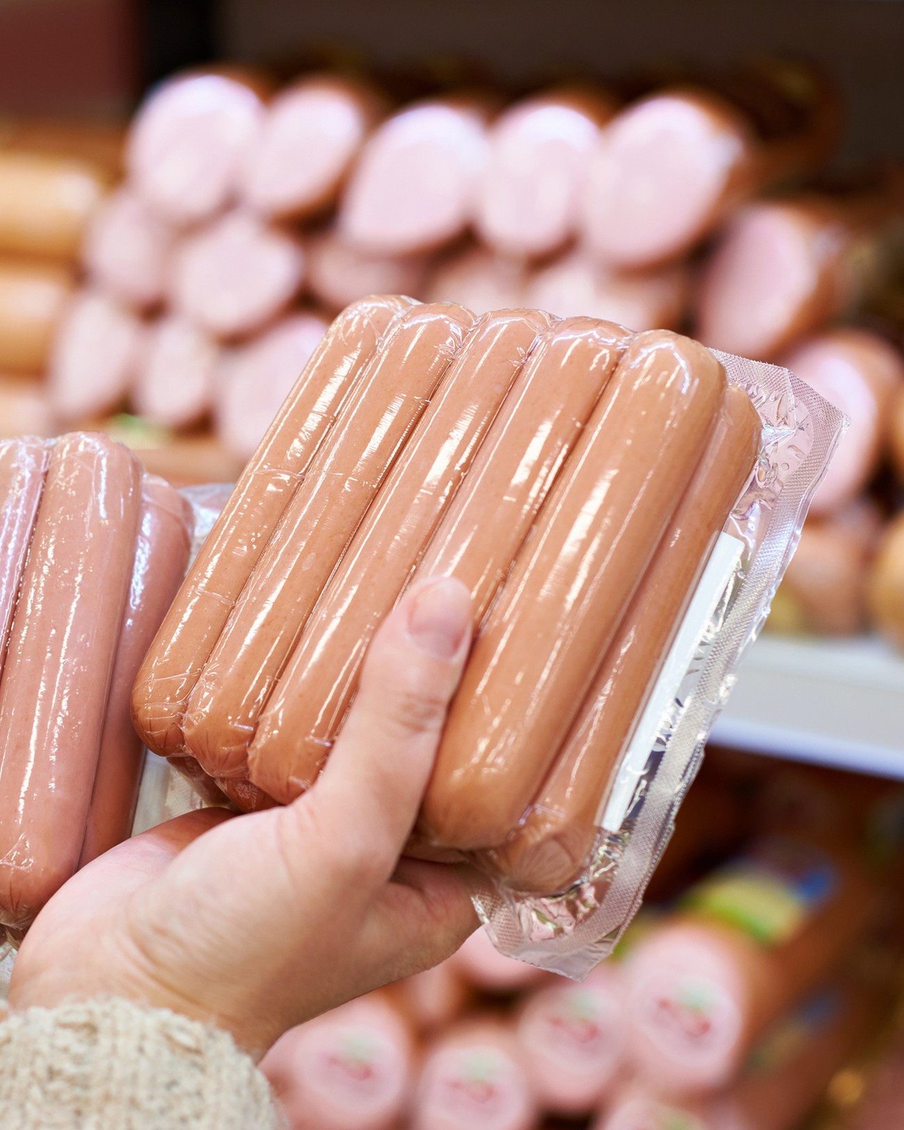 hands holding hot dogs in grocery store