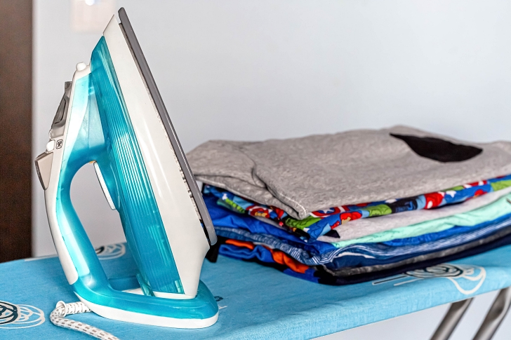 Electric iron on an ironing board with a stack of ironed clothes
