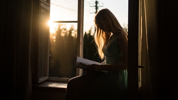woman reading a book indoors at sunset