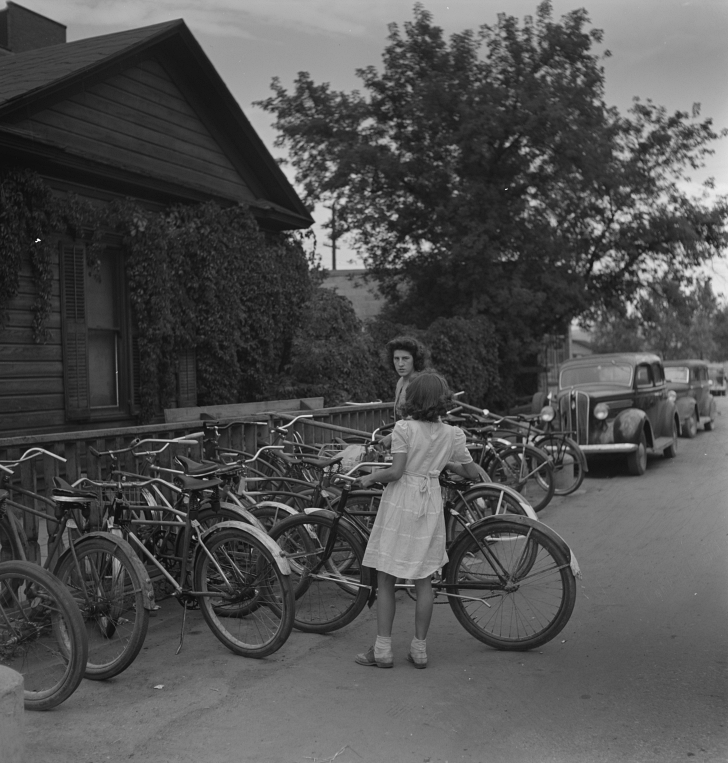 2 girls putting bikes into a bike rack, 1940s