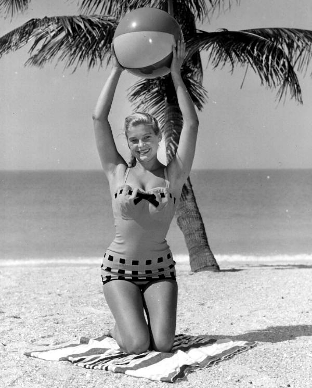 model holding up a beach ball on the beach in 1956