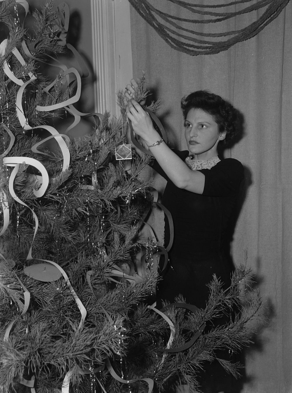 woman decorating a Christmas tree with homemade items 1943