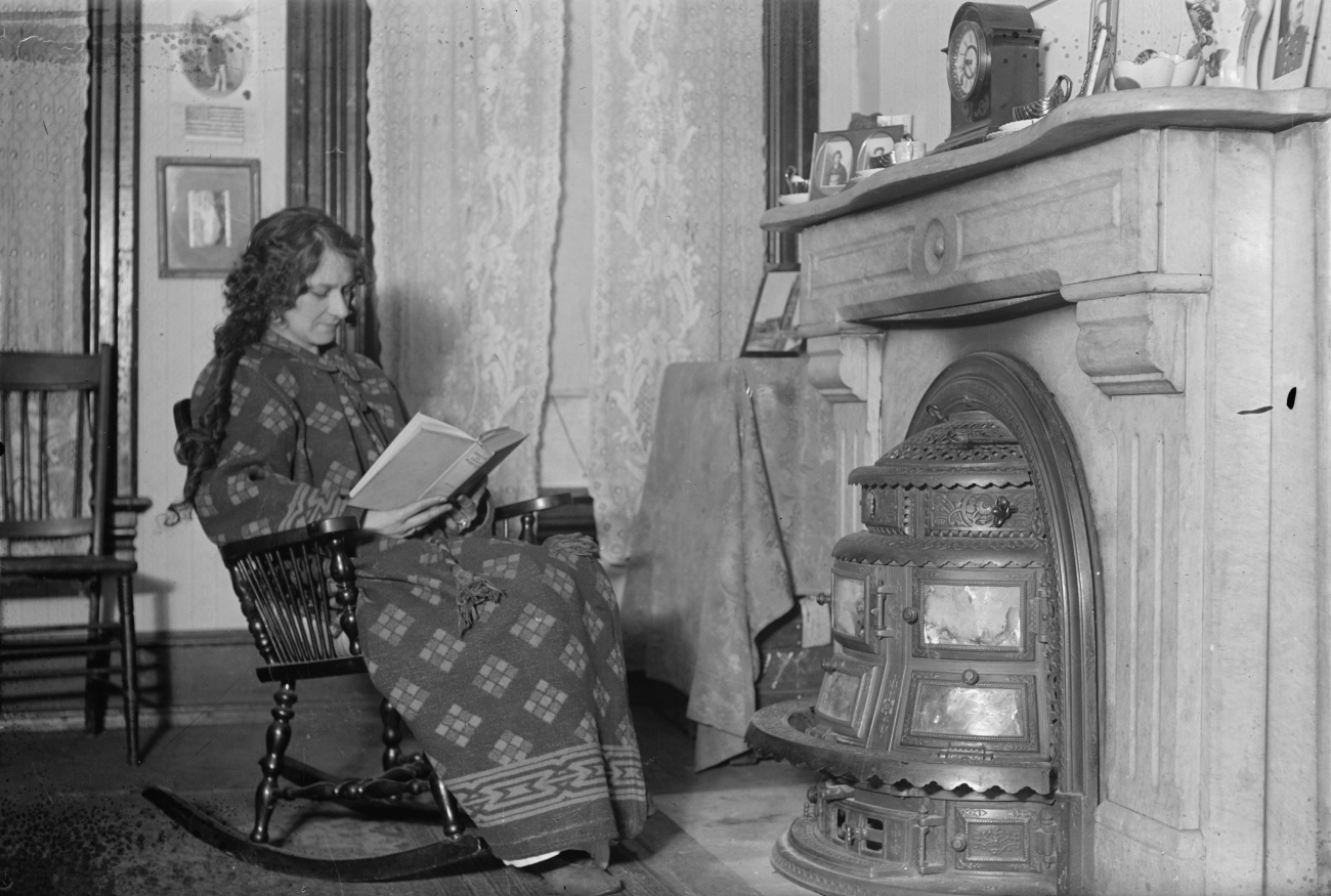 Woman Reading by Stove in Fireplace