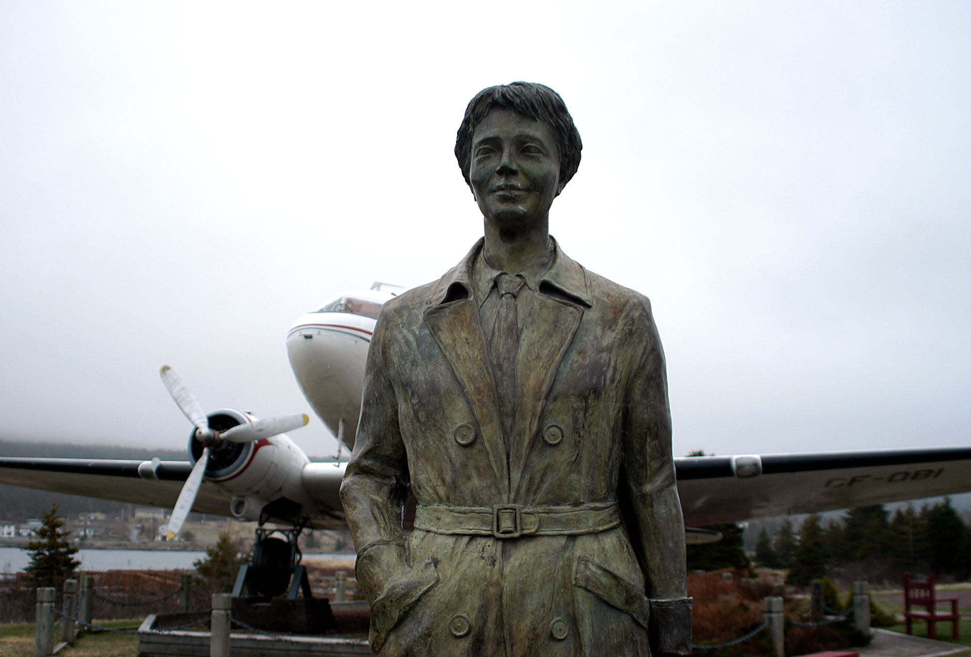 Bronze statue of Amelia Earhart wearing a tie and jacket. Behind her is a white plane and grey sky.