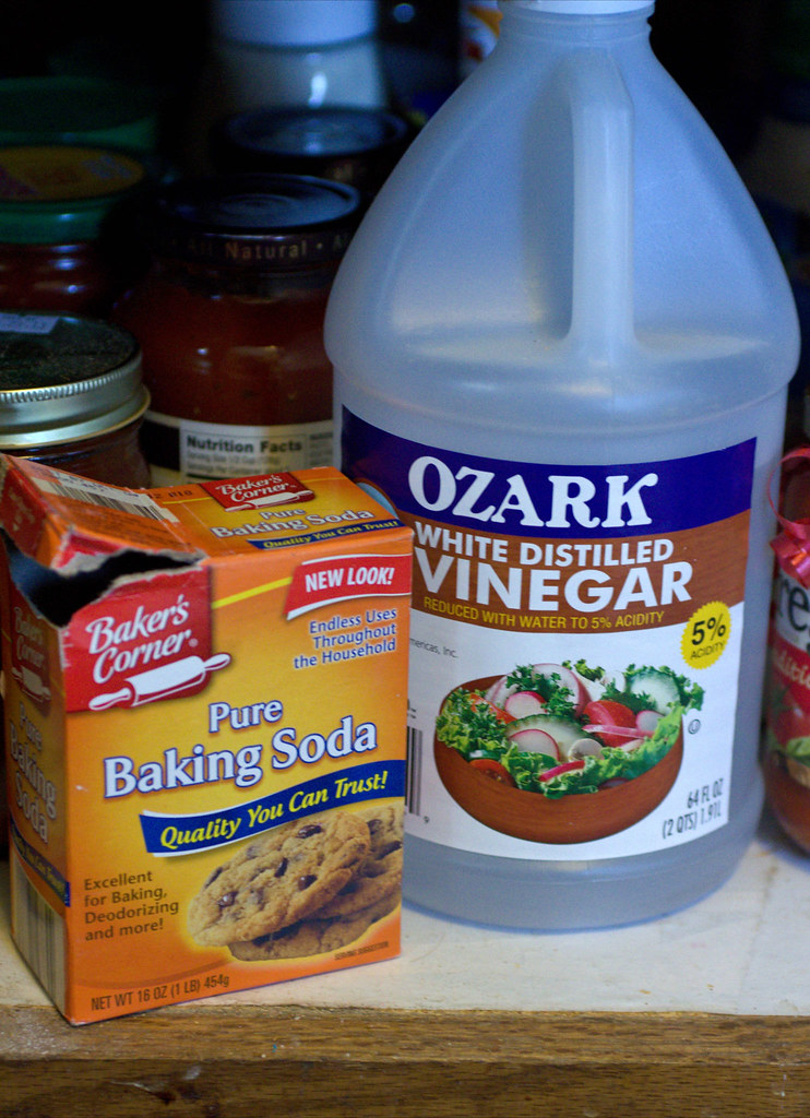 On the left, an orange box reads "Baker's Corner, Pure Baking Soda: Quality you can trust!" On the right, a large opaque plastic jug reads, "OZARK: WHITE DISTILLED VINEGAR."