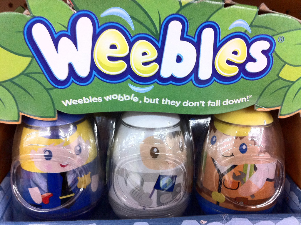 A box with egg shaped weebles inside. The box reads: "Weebles: Weebles wobble, but they don't fall down!" The left figure is a police woman, the middle is an astronaut, and the right figure is a construction worker.