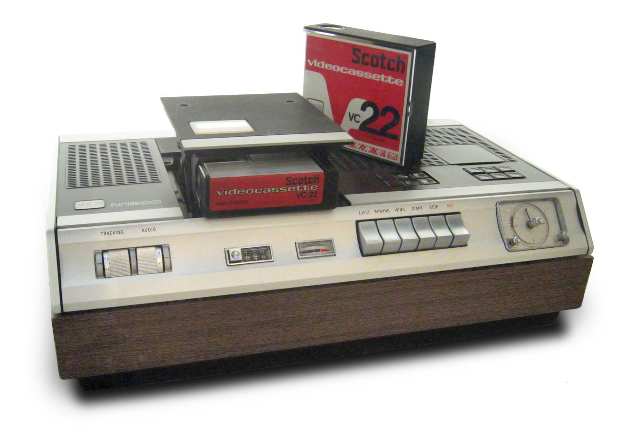 A white and wood VCR machine. The square items placed on top (videocassettes) read: Scotch, videocassette, VC 22