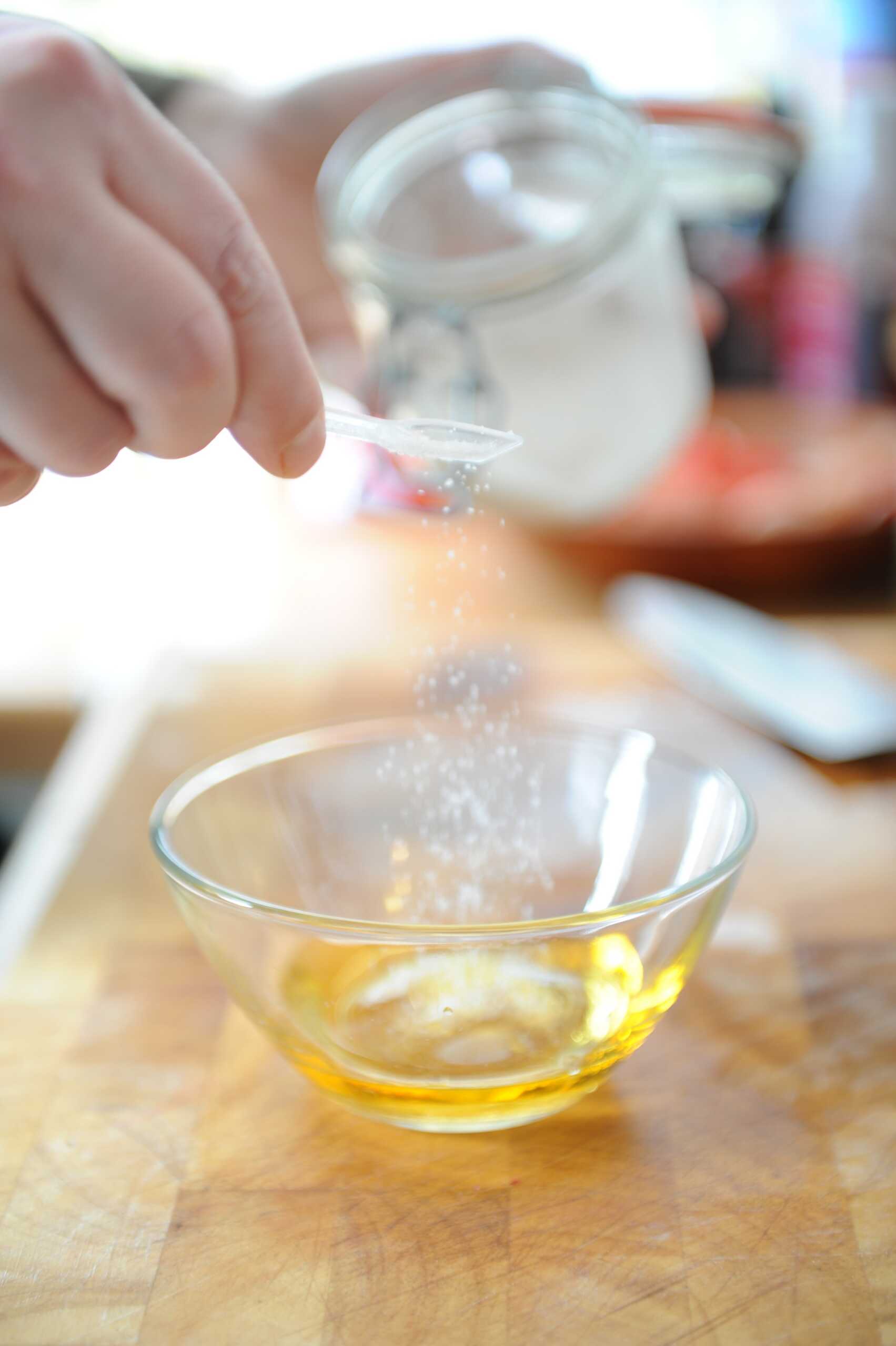 A person sprinkles salt over a bowl of oil, preparing a flavorful mixture for cooking or dressing.