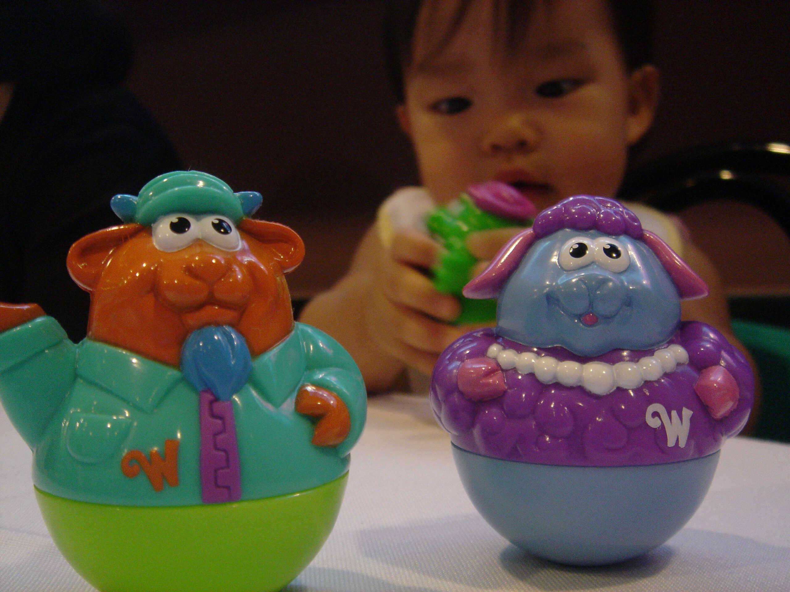 A little kid sits next to a vibrant toy egg (Weeble), looking curious and engaged in playtime.