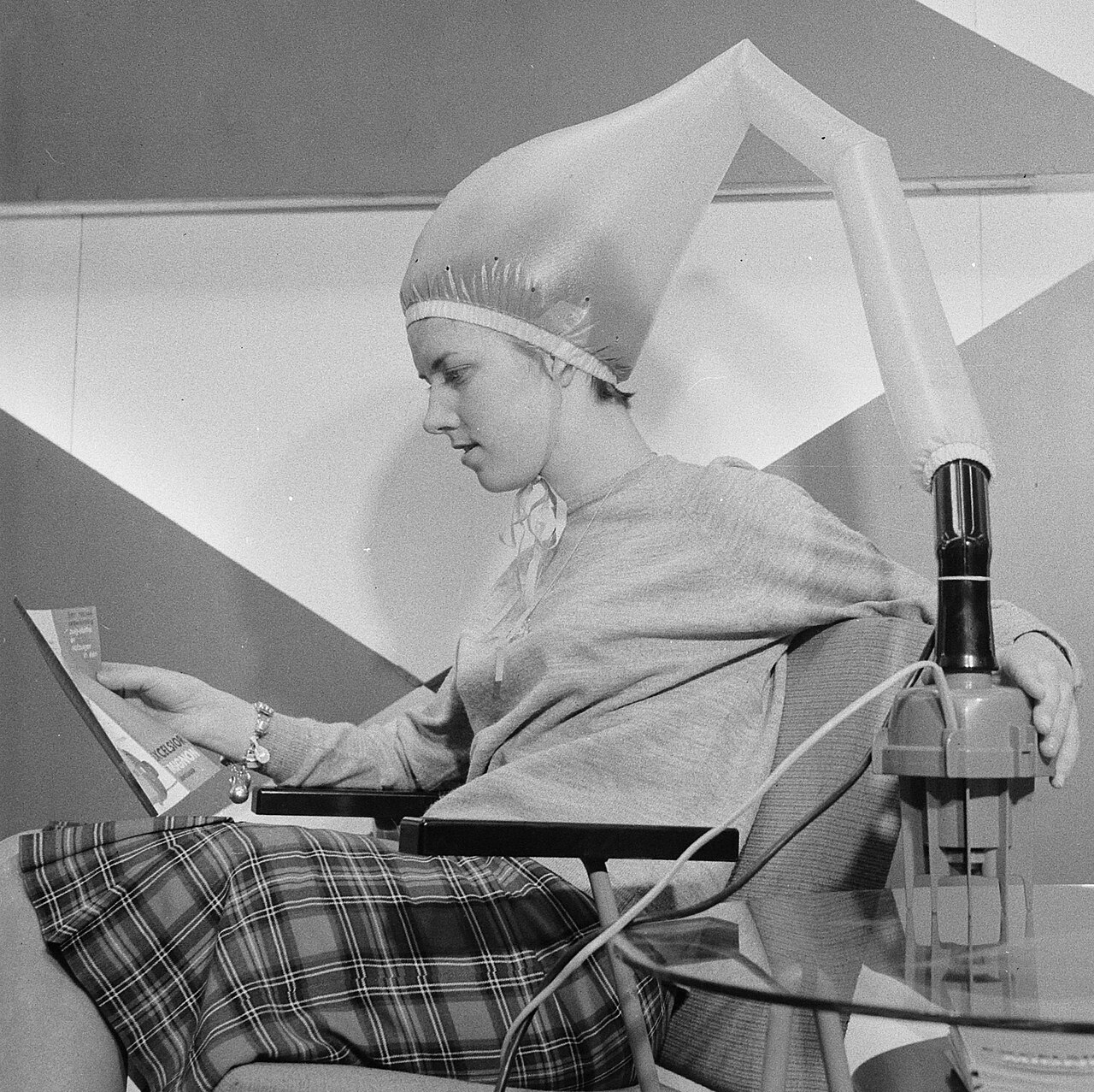 A woman seated in a chair, wearing a hair dryer on her head, appears relaxed during a hair styling session.