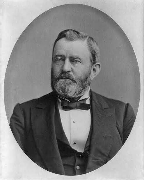 Portrait of General and President Ulysses S. Grant. He has a beard and wears a suit with bow tie.