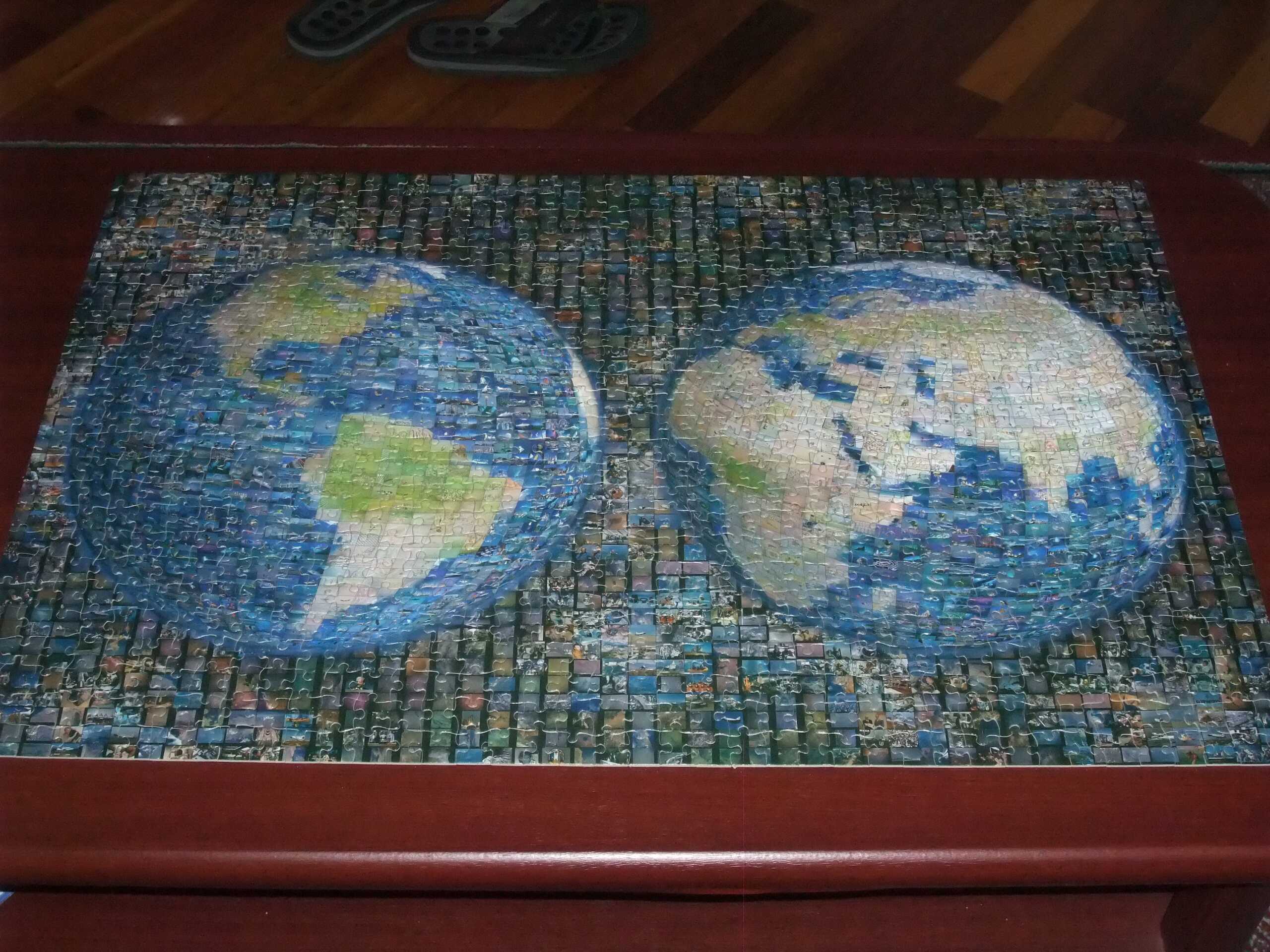A completed jigsaw puzzle featuring two vibrant world maps, showcasing the globe's diverse landscapes on a wooden table.